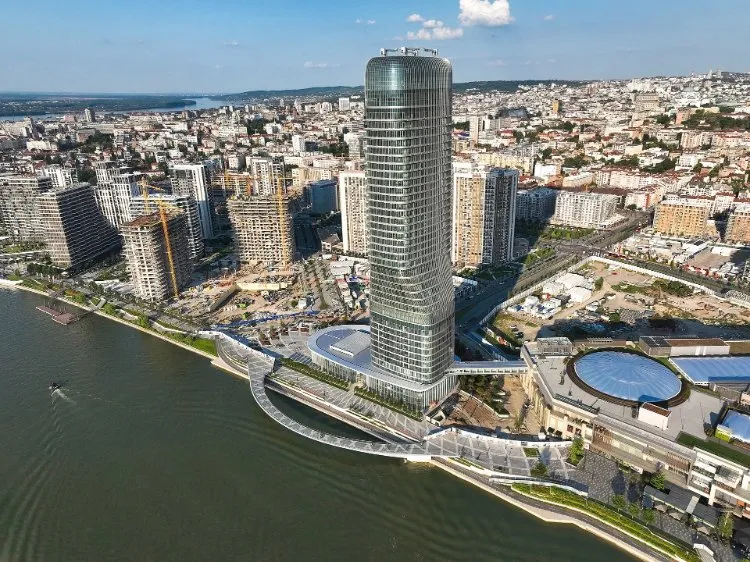 An aerial view of the Belgrade Waterfront district on the Sava, with its tall glass tower, new apartment blocks and the old town on the hill behind.