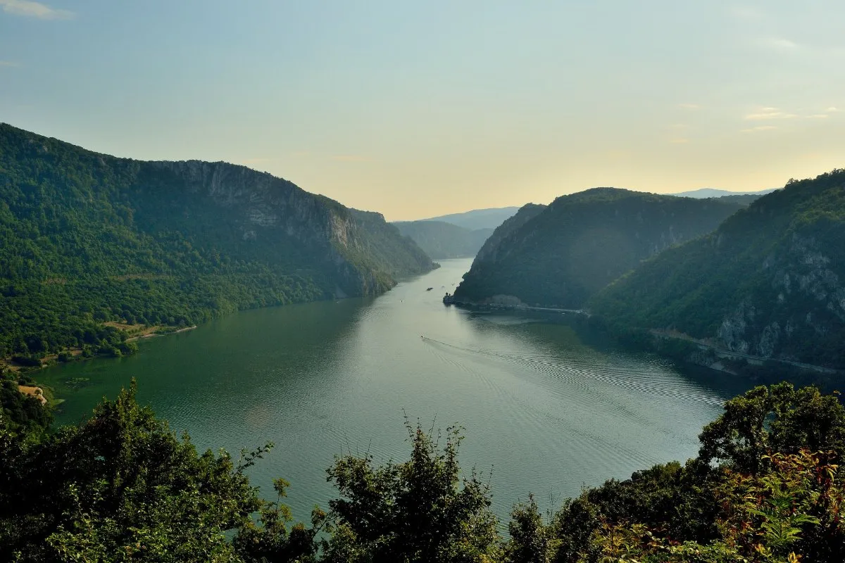 A view from above of the Danube narrowing between forested mountains in the Kazan part of the Đerdap gorge, in soft evening light.