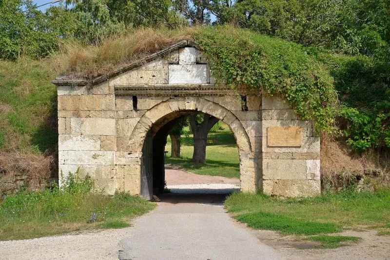 An old stone gate of the Fetislam Fortress in Kladovo, covered with grass and ivy, with a path through its arch to the trees behind.