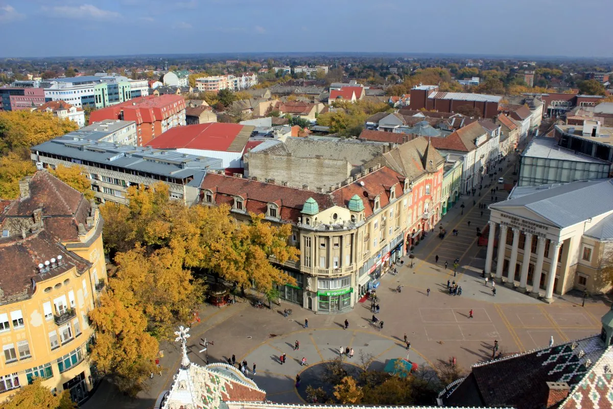 A view from the City Hall tower over the centre of Subotica in autumn, with the pedestrian street, the columned National Theatre and red roofs to the flat horizon.